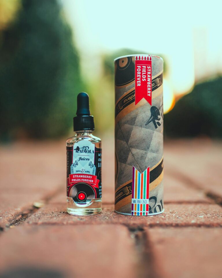 Close-up of vape juice bottle and packaging on brick floor with blurred background.